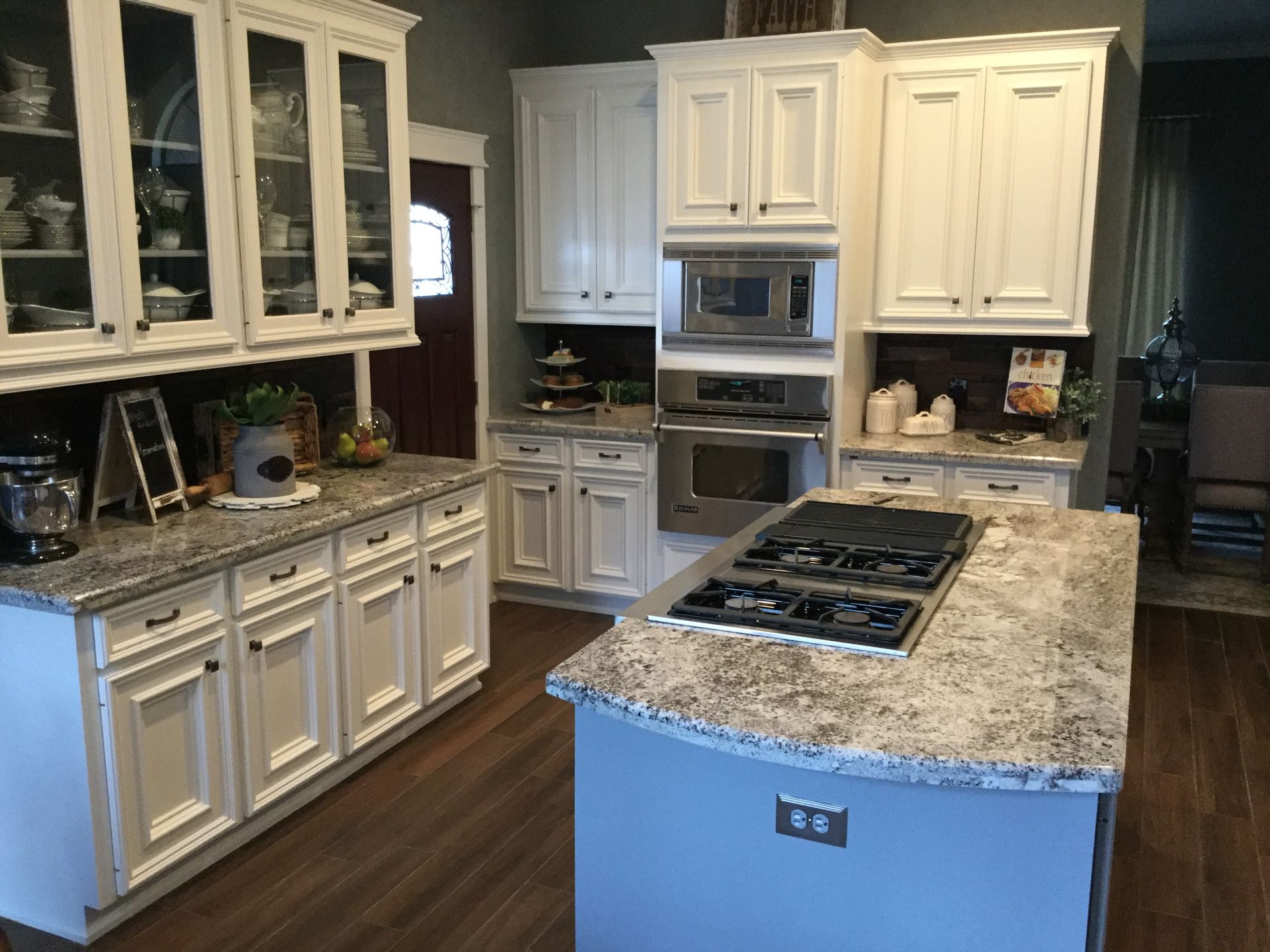 White kitchen with granite countertops, stainless steel appliances, and island with stovetop.