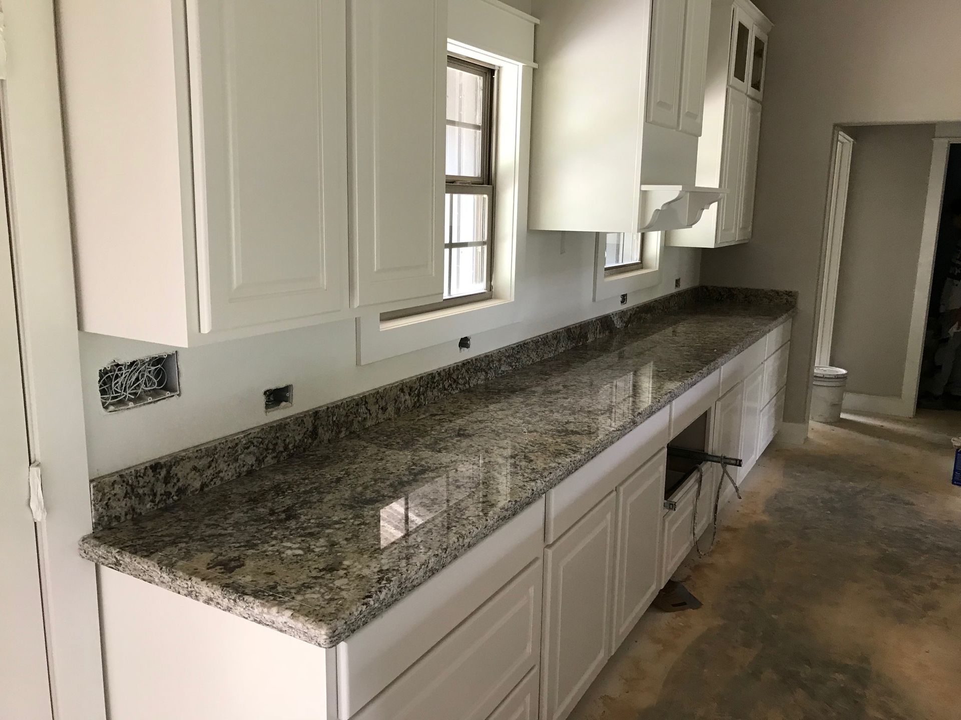 White kitchen cabinets with granite countertop near a window.