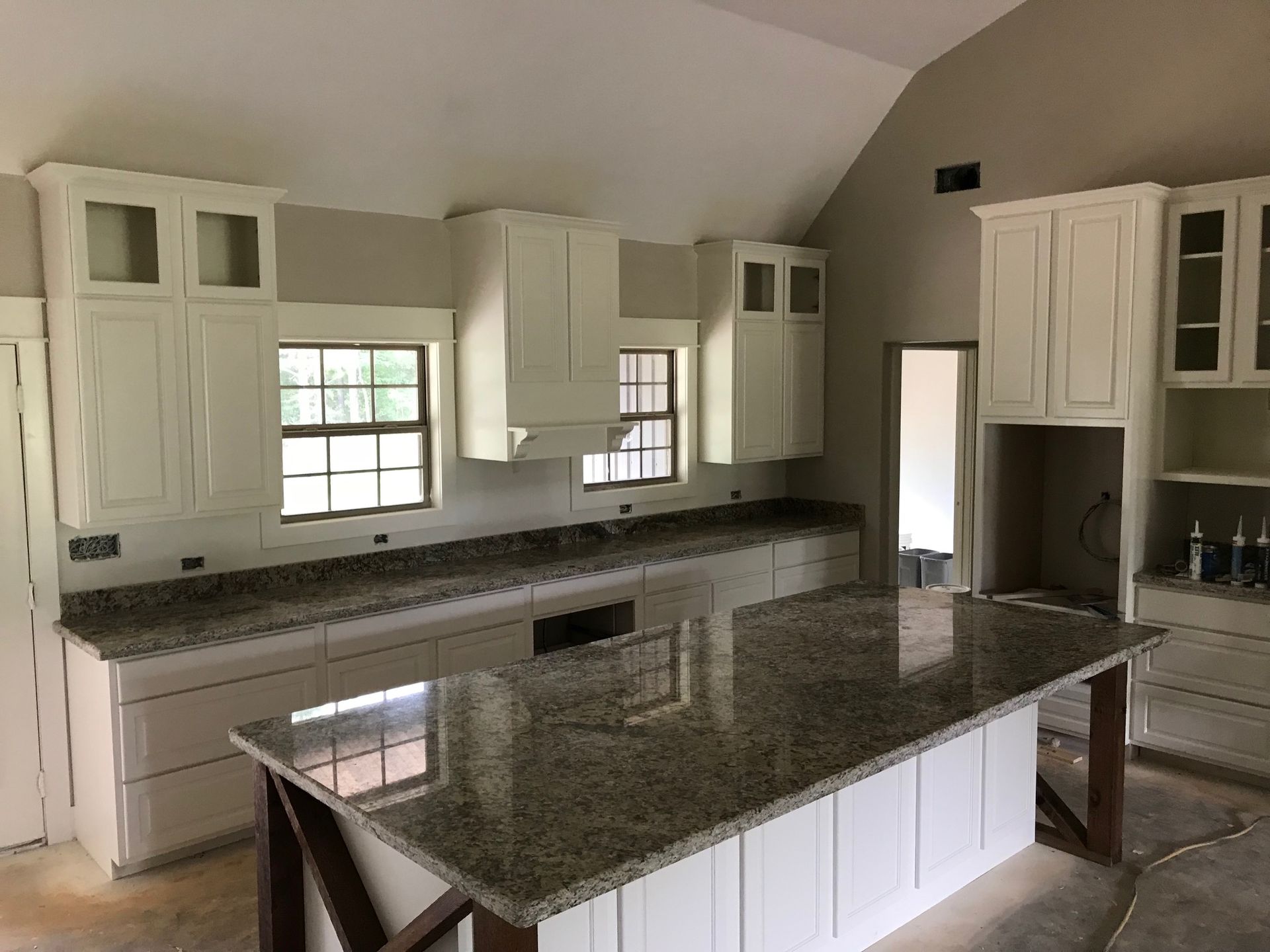 White kitchen with granite countertops, island with wood supports, cabinets, and windows.