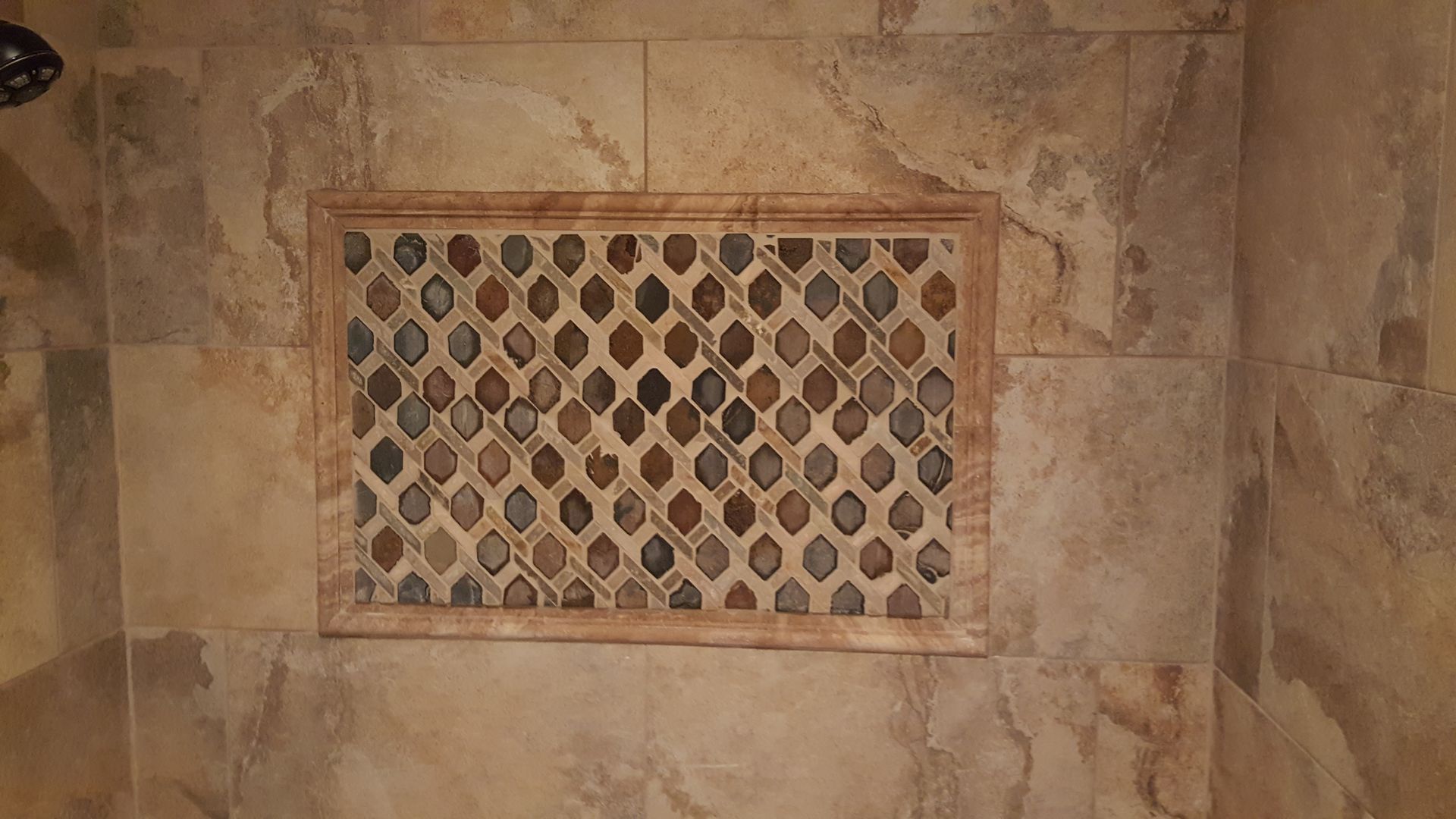 Shower niche with decorative stone inlay, surrounded by neutral-toned tile.