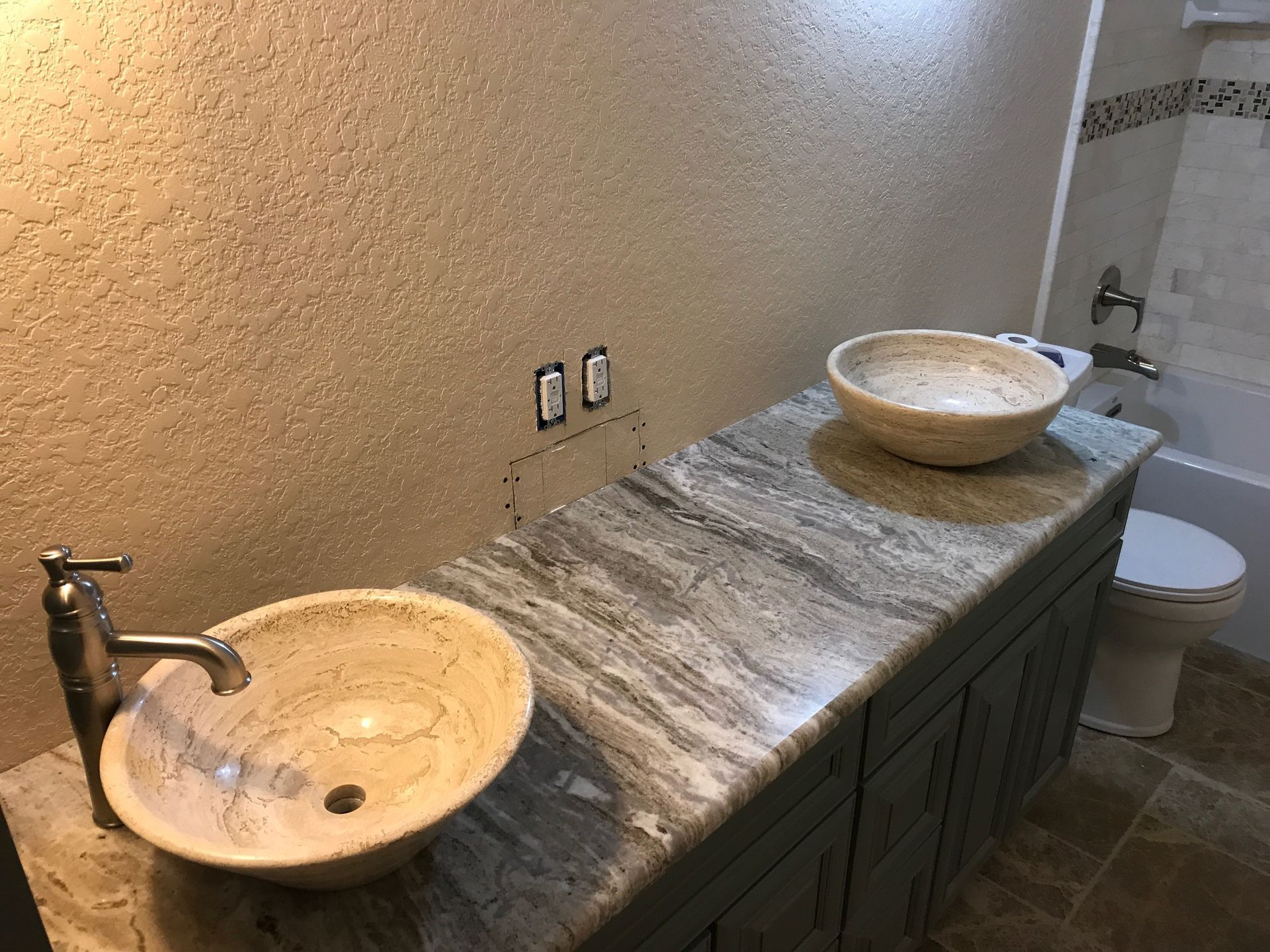 Bathroom with two vessel sinks on a marble countertop, set against a textured wall and cabinet.