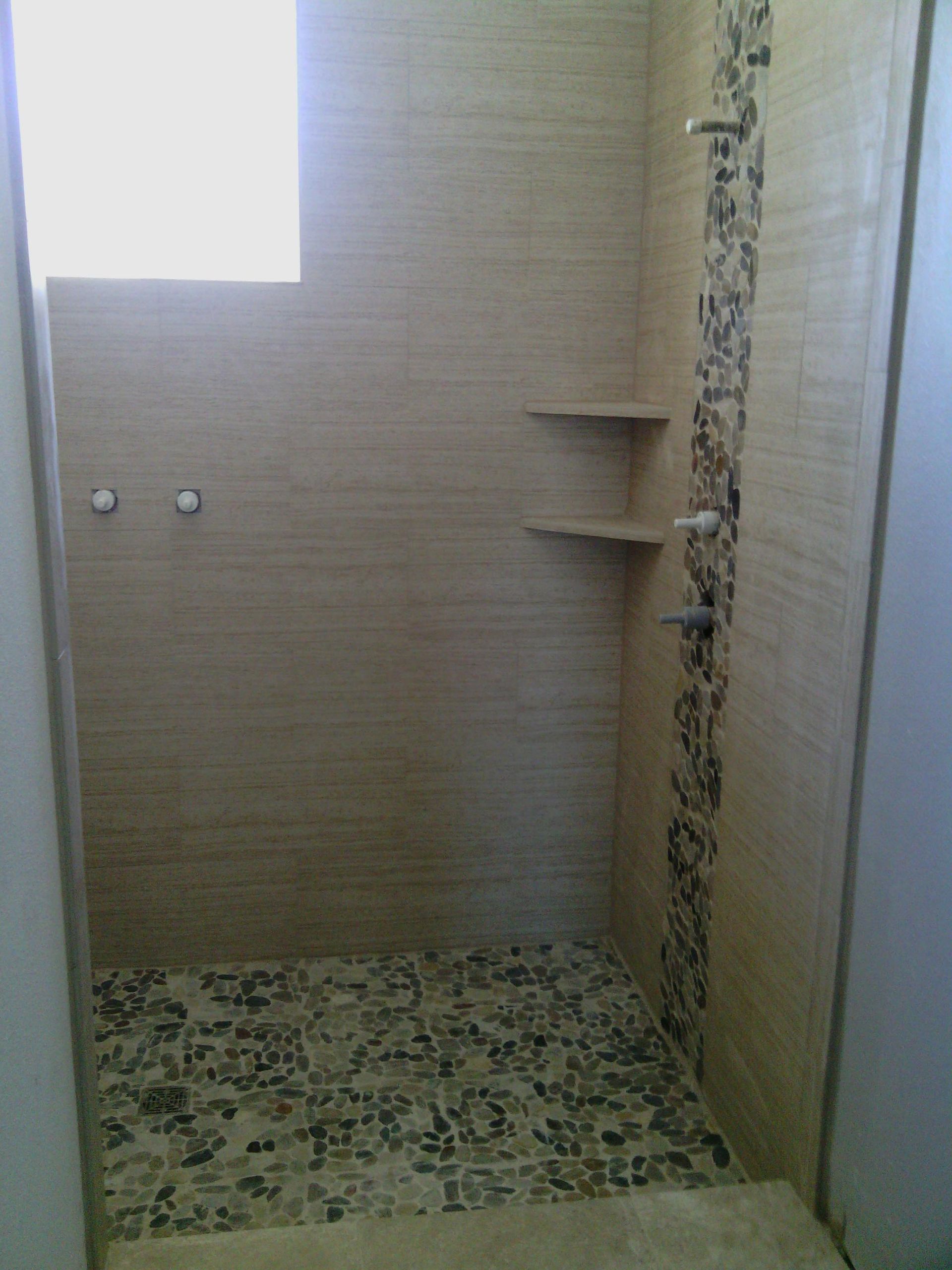 Shower with pebble floor, beige tile walls, a decorative strip, and built-in shelves.