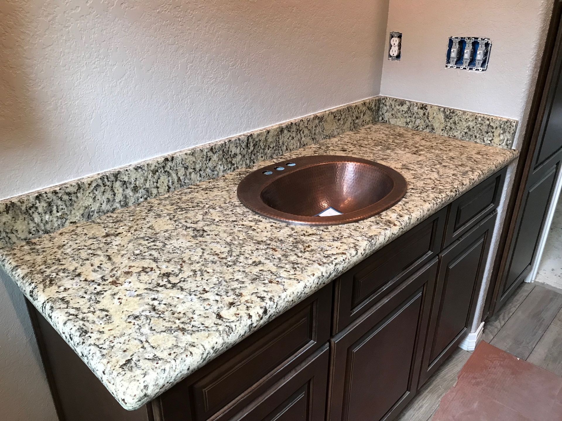 Bathroom vanity with copper sink, granite countertop, and dark brown cabinets.