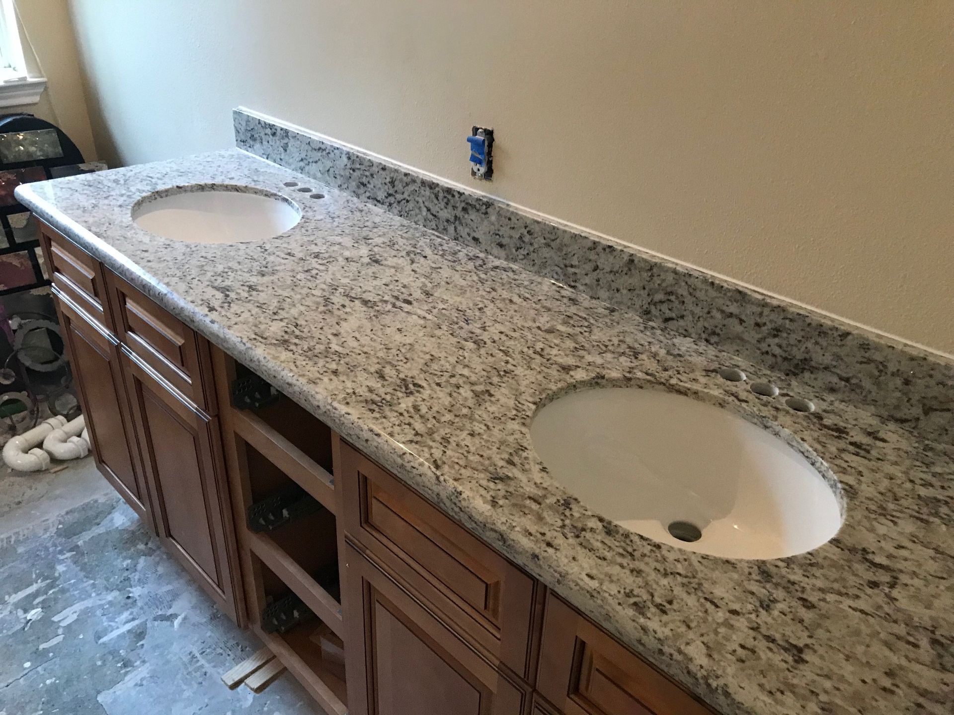 Bathroom vanity with a granite countertop and two sinks, with cabinets and unfinished wall.
