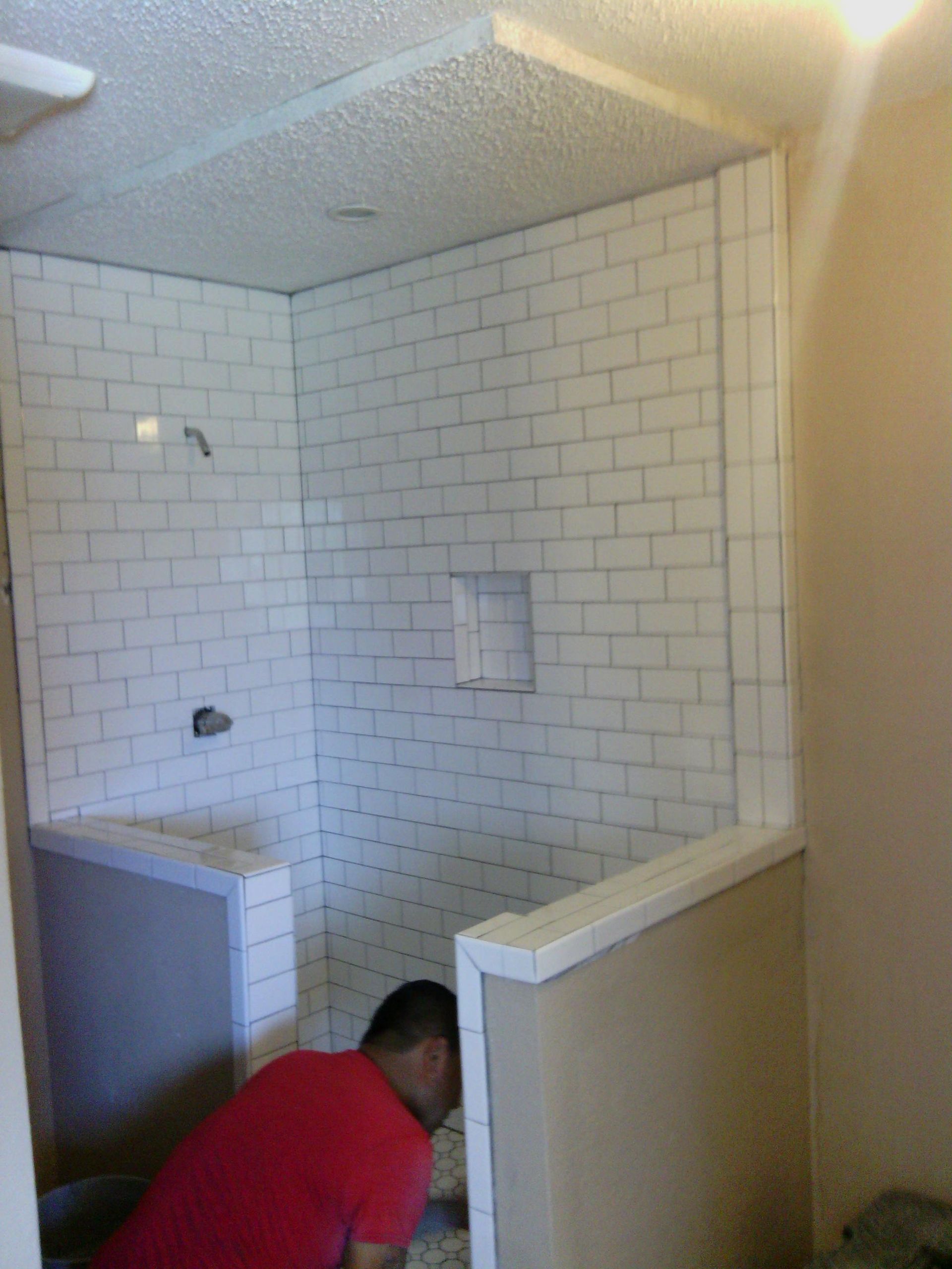 Person tiling a shower with white subway tiles.