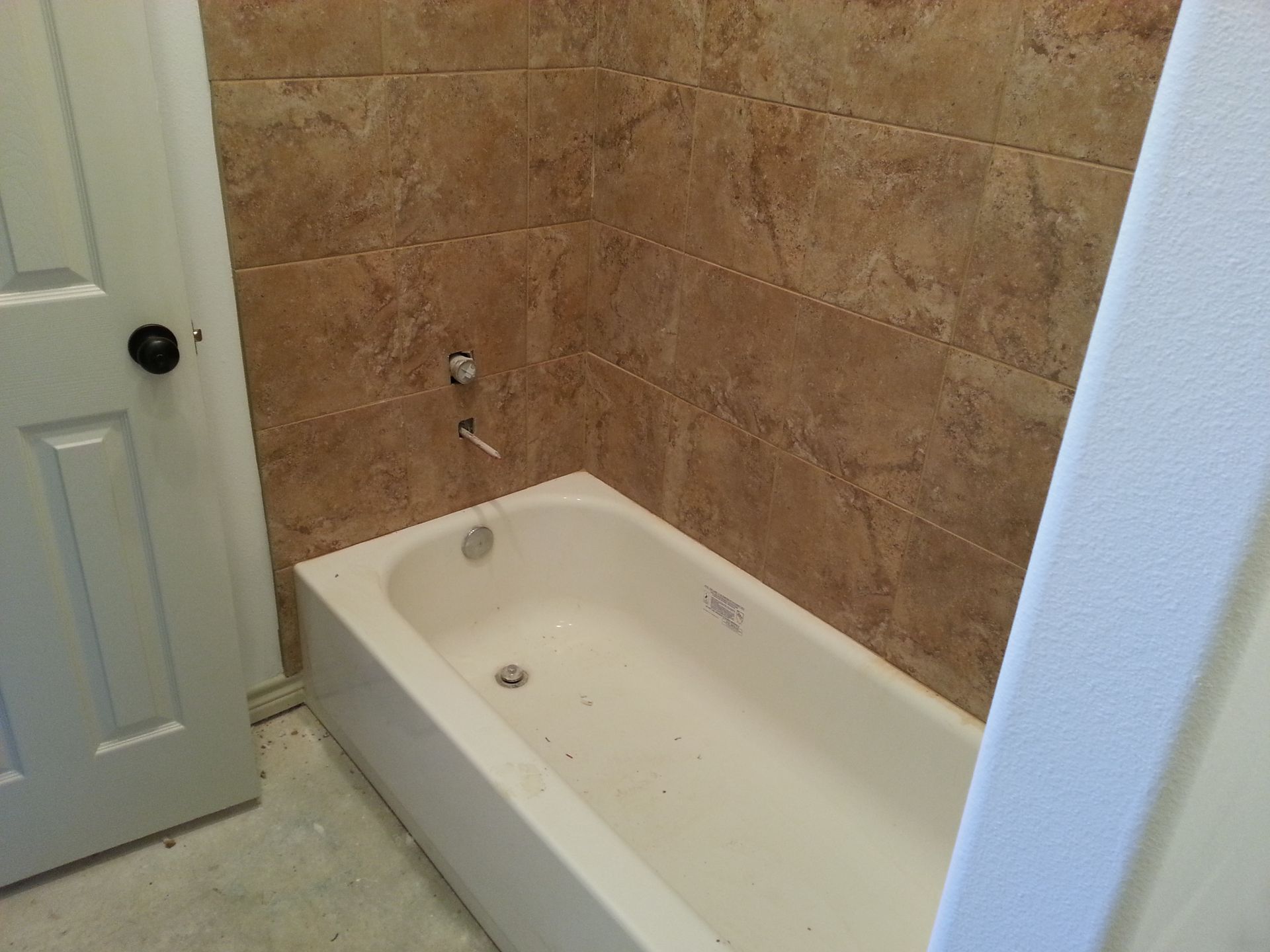 White bathtub with brown tile surround, next to a partially visible white door and wall.