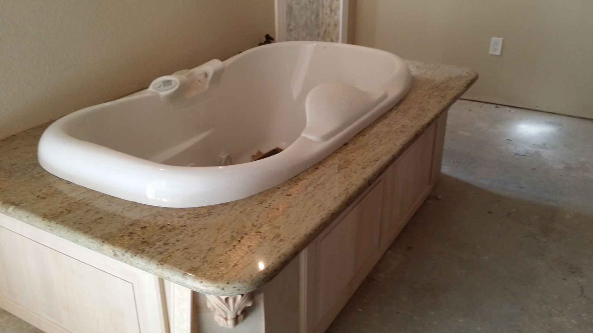 White bathtub installed on a granite countertop, built-in to light wood cabinetry in a room with neutral walls.