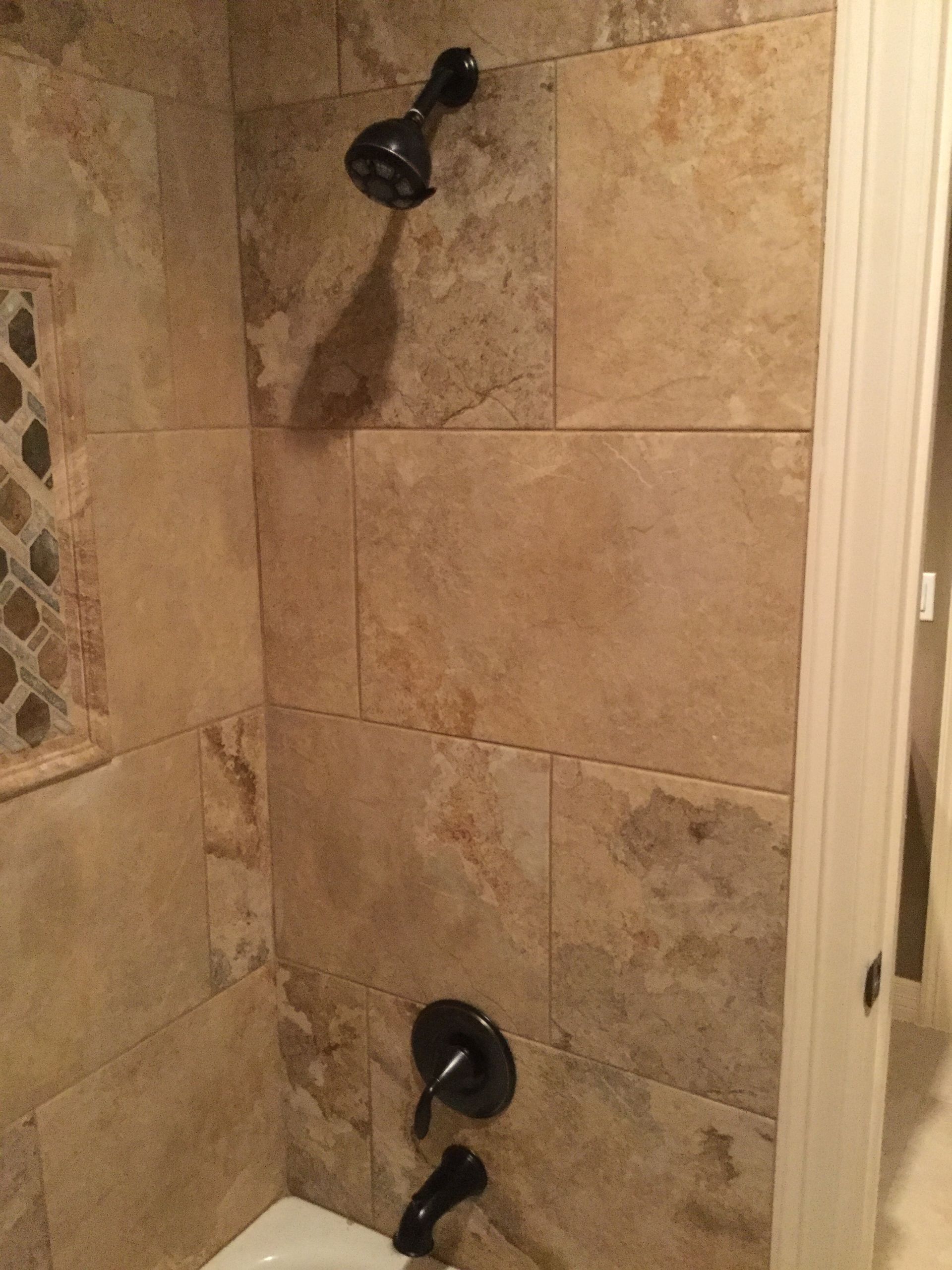 Shower with brown tile walls, black showerhead and faucet.