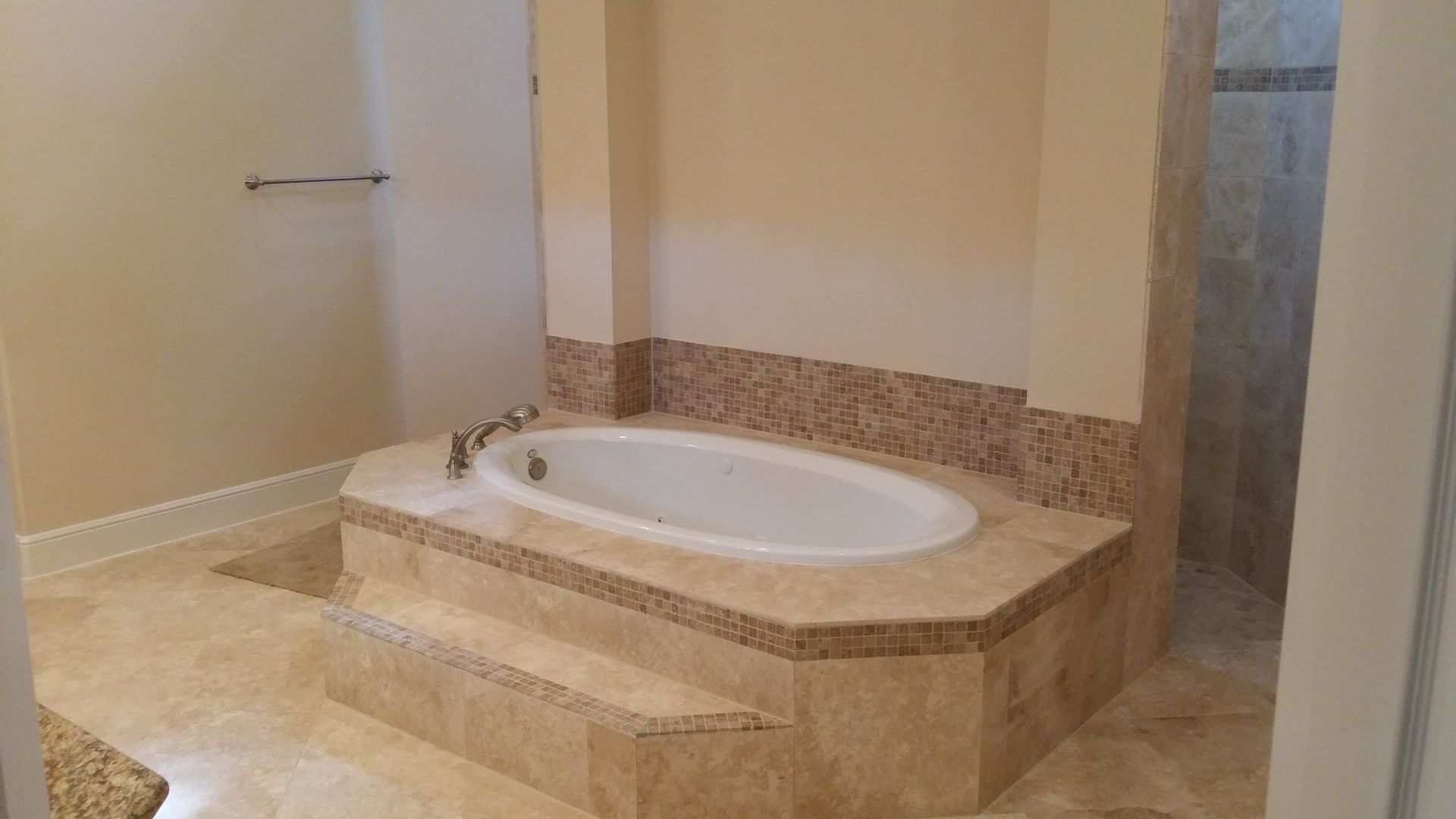 Bathroom with oval bathtub in a raised stone enclosure. Beige walls and flooring.