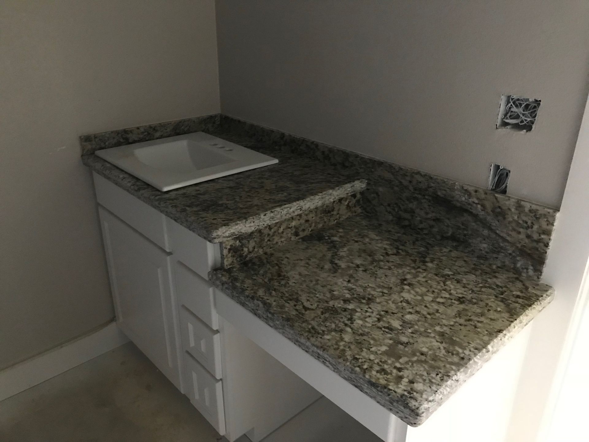 White cabinet with granite countertop, built-in sink. Wall-mounted electrical outlets visible.