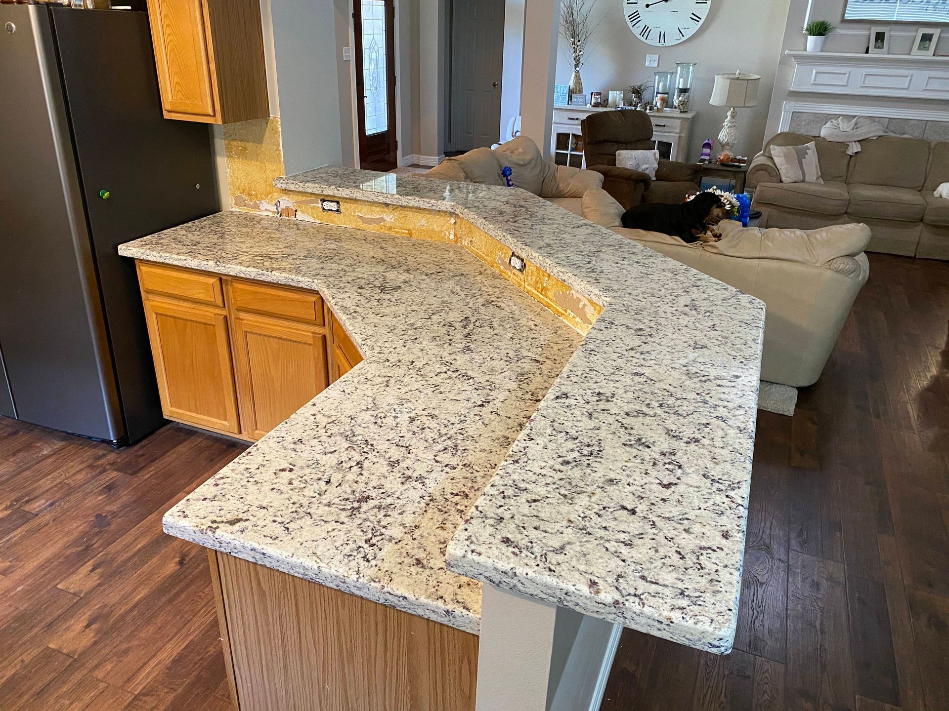 Granite countertop in a kitchen with wooden cabinets and a dark refrigerator.