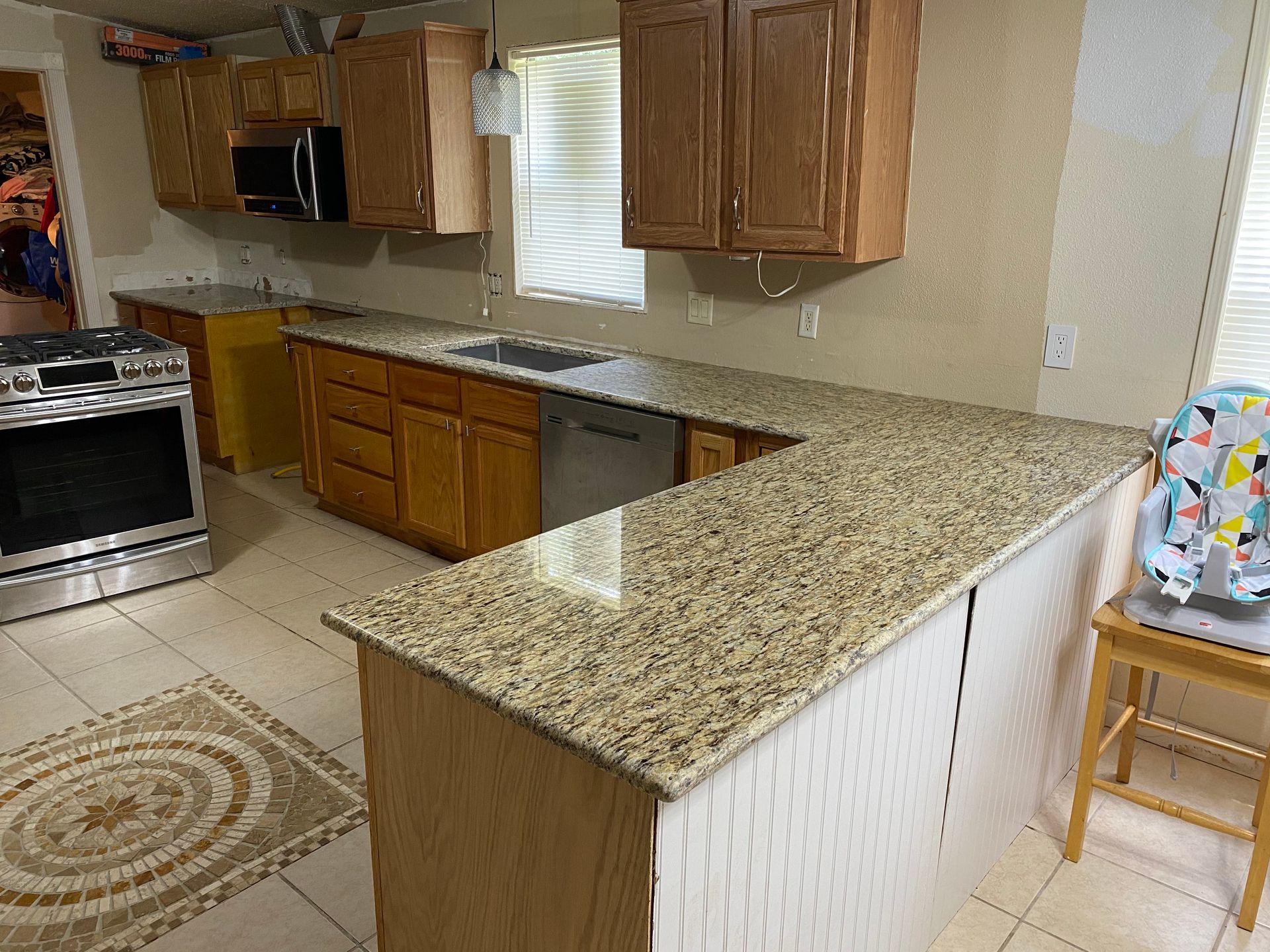 Kitchen with light-colored granite countertops, wooden cabinets, stainless steel appliances, and a tile floor.