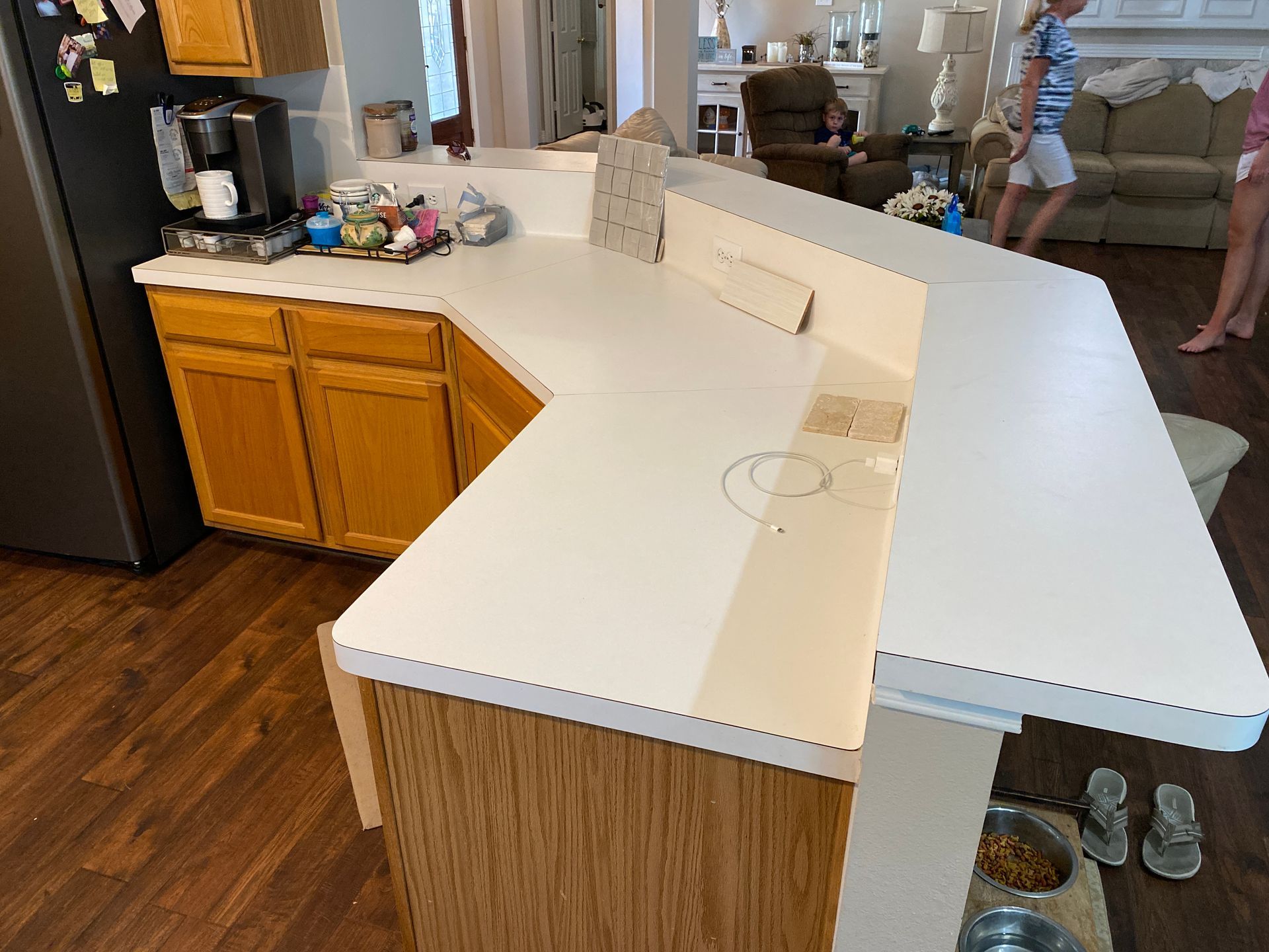 White L-shaped kitchen island with wood cabinets and a sink, viewed from a dining area into a living room.