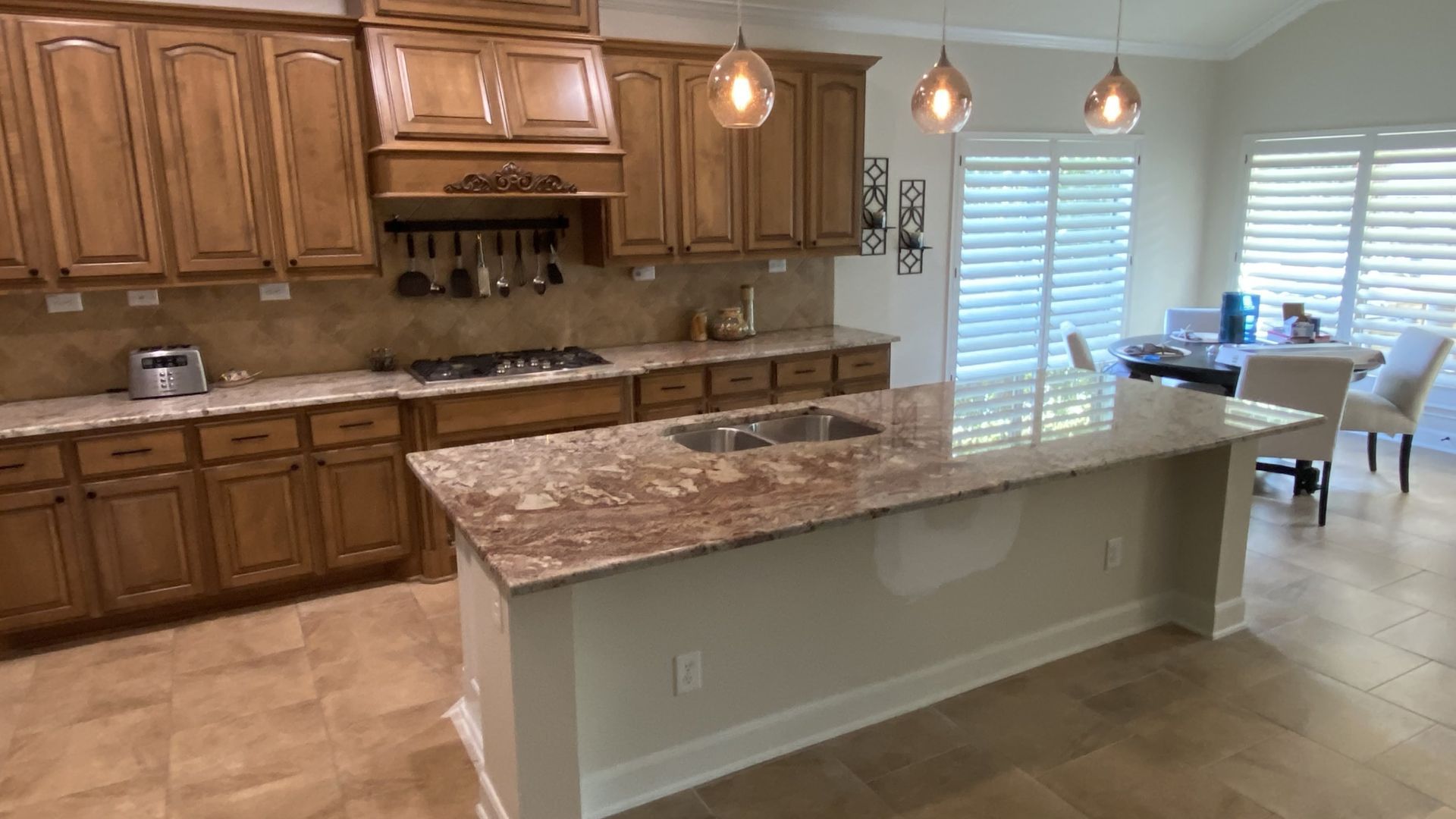 Kitchen with wood cabinets, granite countertops, island with sink, and dining area with shuttered windows.