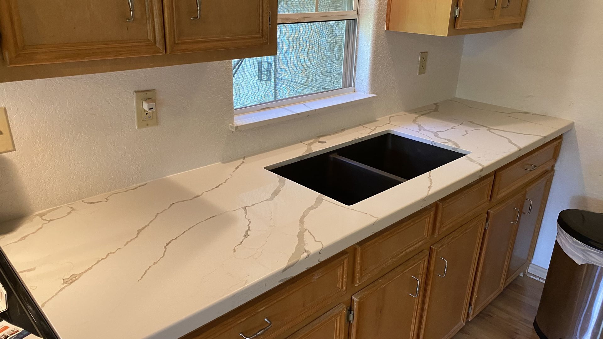 Kitchen countertop with white marble-look surface and black double sink under a window