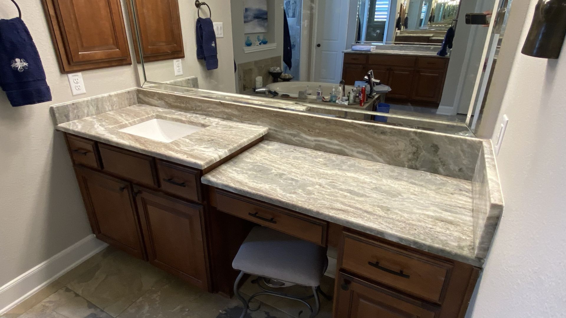 Bathroom vanity with granite countertop and dark wood cabinets, stool and mirror.
