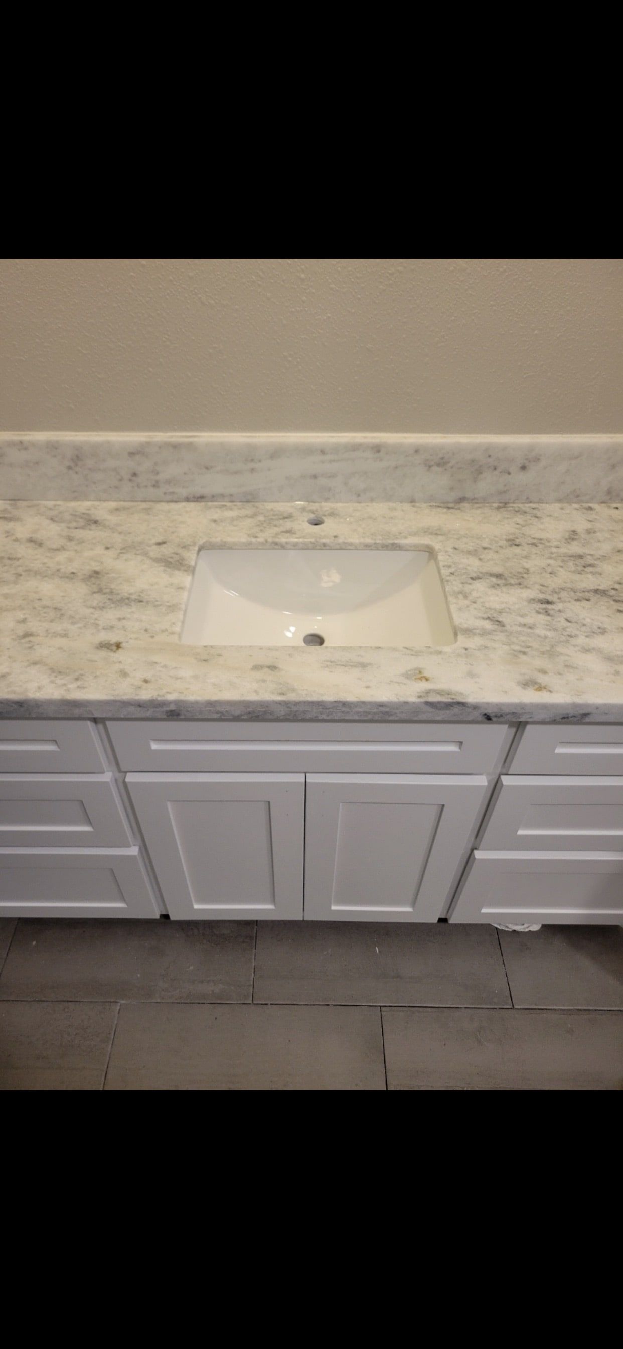 White bathroom vanity with marble countertop and a rectangular sink basin.