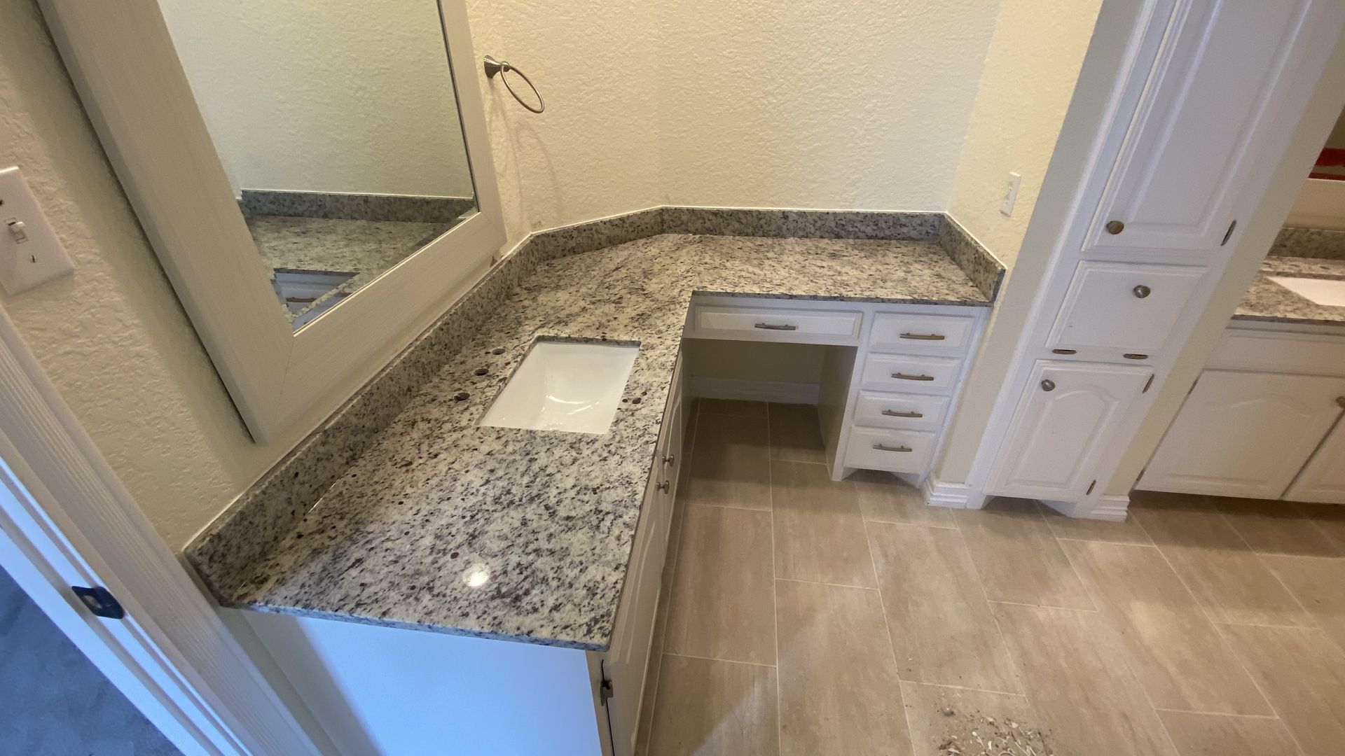 Bathroom with granite countertop, white cabinets, and mirror.