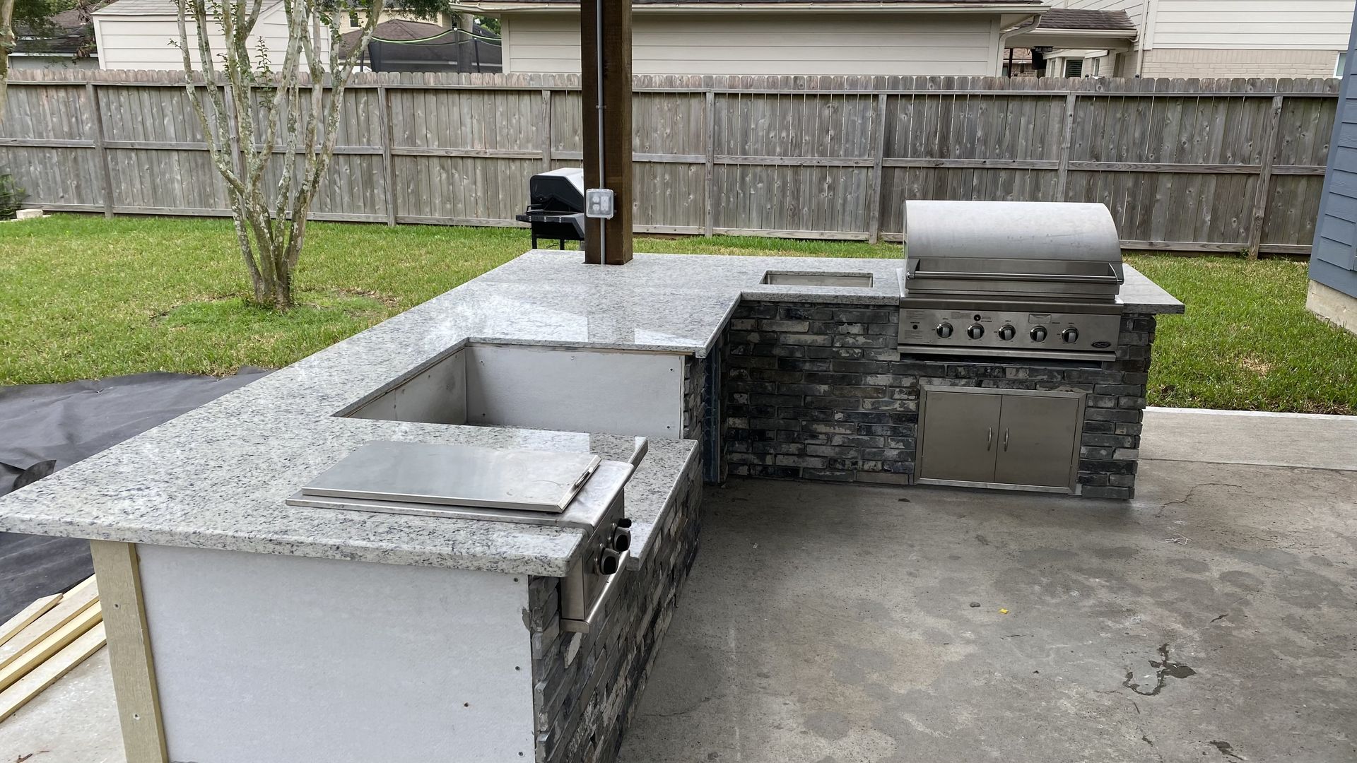 Outdoor kitchen island with grill, sink, and granite countertop, built on a concrete patio.