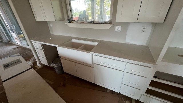 Modern kitchen with white cabinets, beige countertops, window above sink, and brown floor.