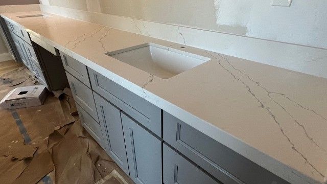 A kitchen with white counter tops and gray cabinets and a sink.