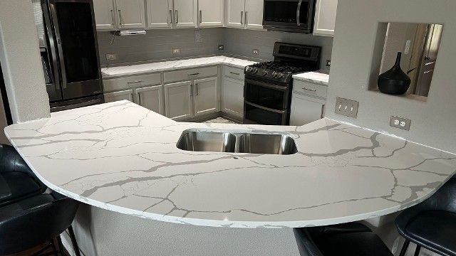 A kitchen with a marble counter top and a stainless steel sink.