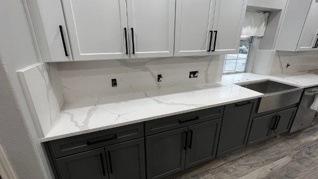 A kitchen with gray cabinets , white counter tops , and a sink.