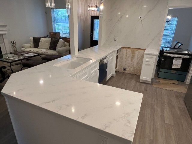 A kitchen with white counter tops and a couch in the background.