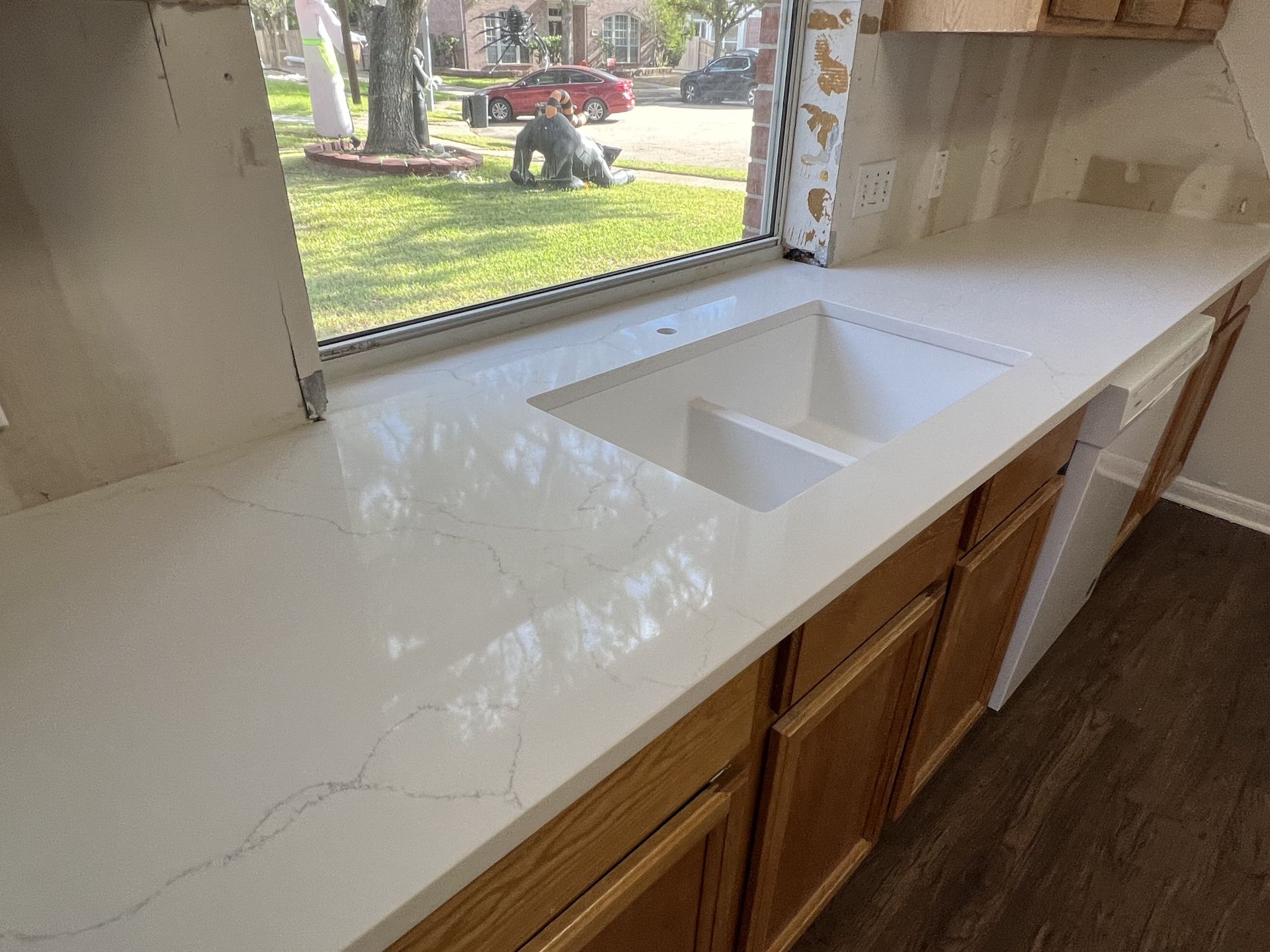 Kitchen countertop with white sink and wooden cabinets beneath a window