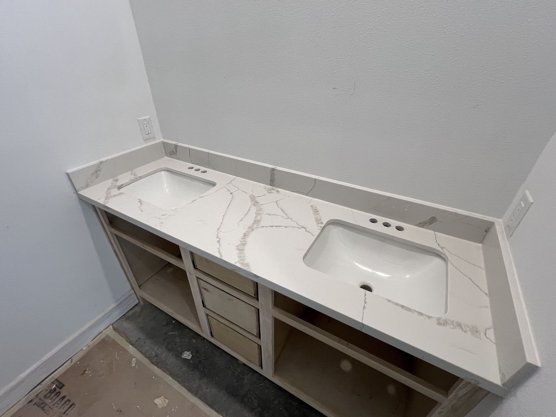 Unfinished bathroom vanity with white countertop and sink installed in a small corner space.