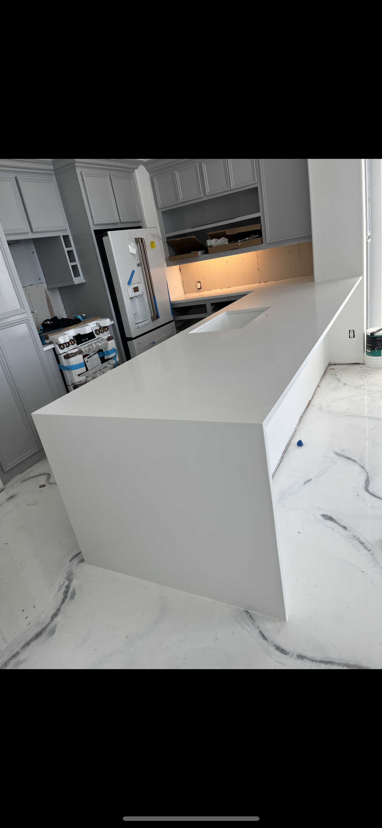 Modern kitchen with a white island, gray cabinets, marble floor, and warm under-cabinet lighting.