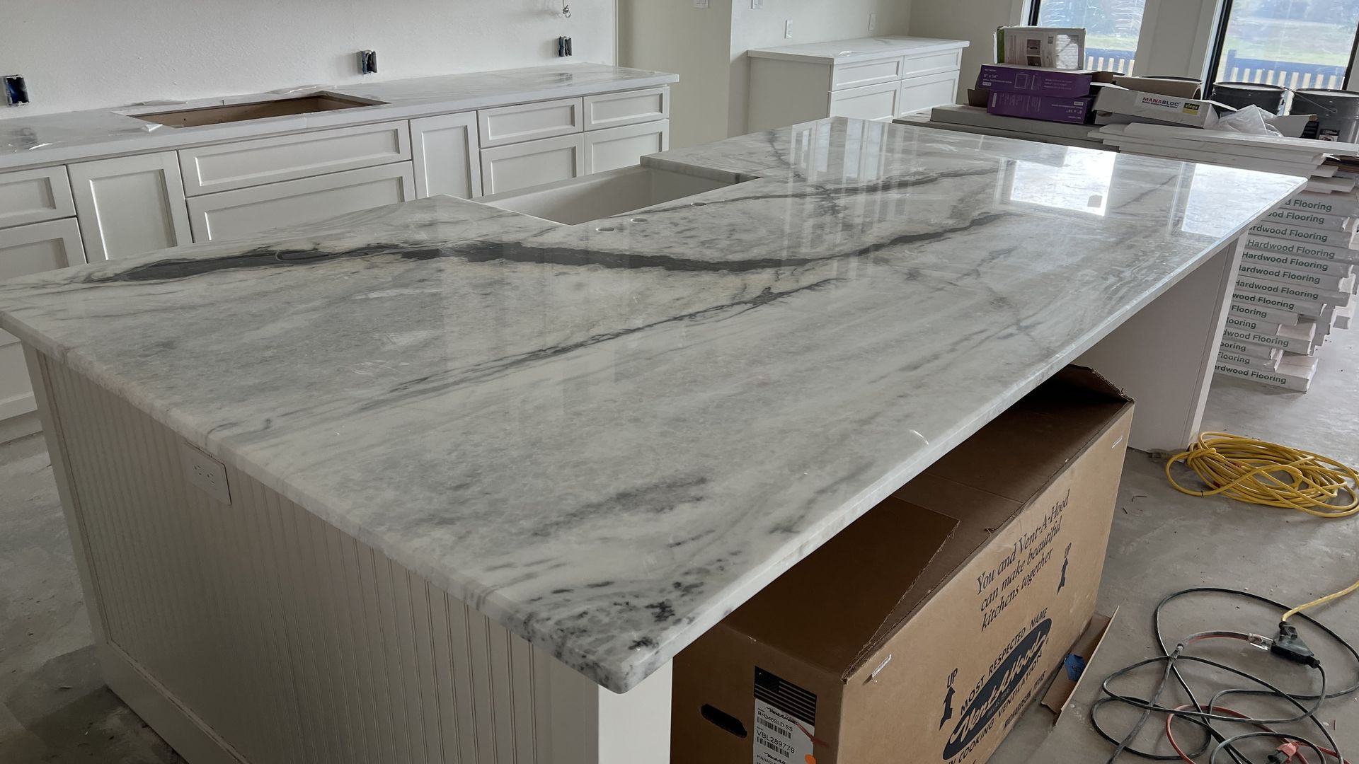 White kitchen island with grey marble countertop and built-in sink. Brown cardboard box beneath the island.