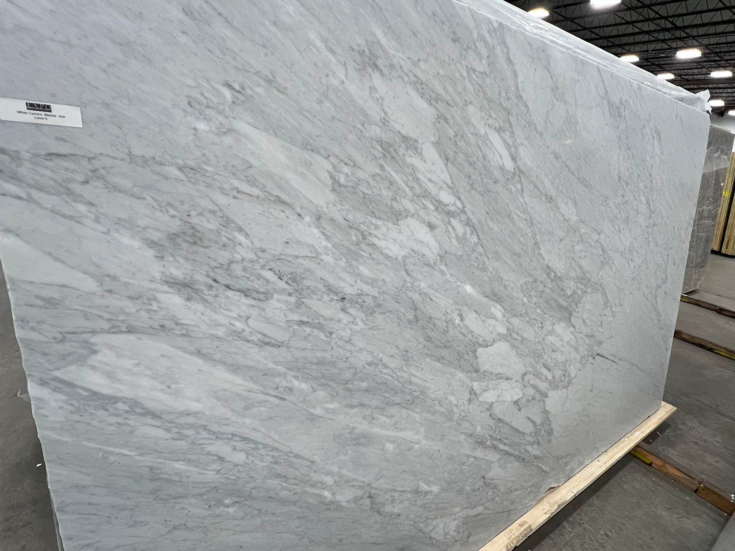 Large slab of white and gray marble, veined, displayed in a warehouse setting.