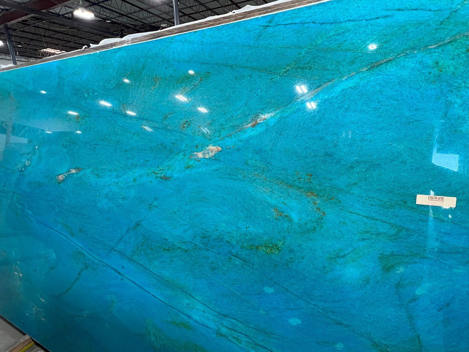Large slab of vibrant blue-green stone with gold and brown veining, in a warehouse setting.