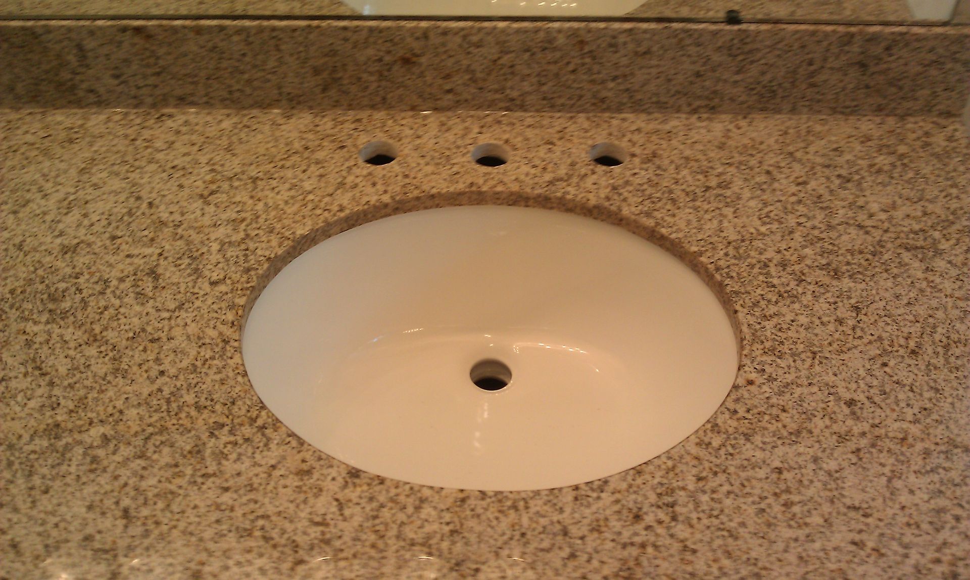 White oval sink in a speckled granite countertop. Three faucet holes.