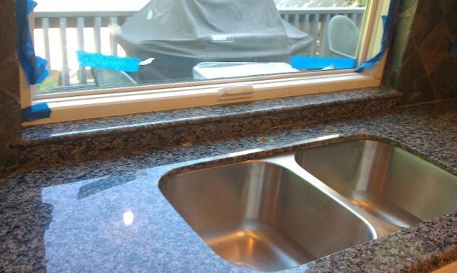 A kitchen sink with granite countertops and a window view of an outdoor patio.