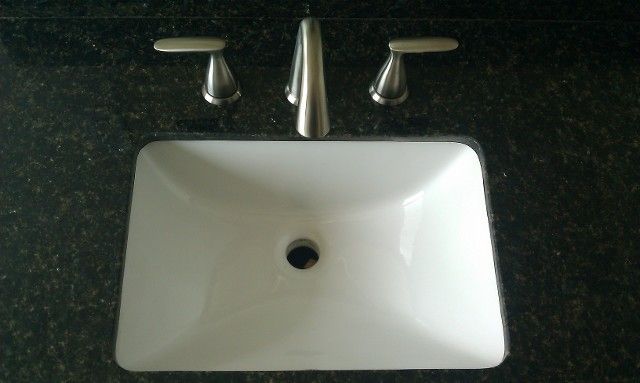 White rectangular sink with faucet and handles on dark countertop.