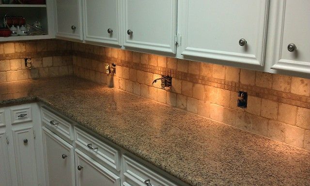 Kitchen with white cabinets, beige granite countertop, and tile backsplash, under cabinet lighting.