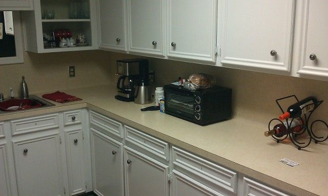 White kitchen cabinets with appliances on a beige countertop, including a coffee maker and toaster oven.