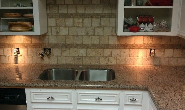 Kitchen with white cabinets, stone backsplash, double sink, granite countertop, and under-cabinet lighting.