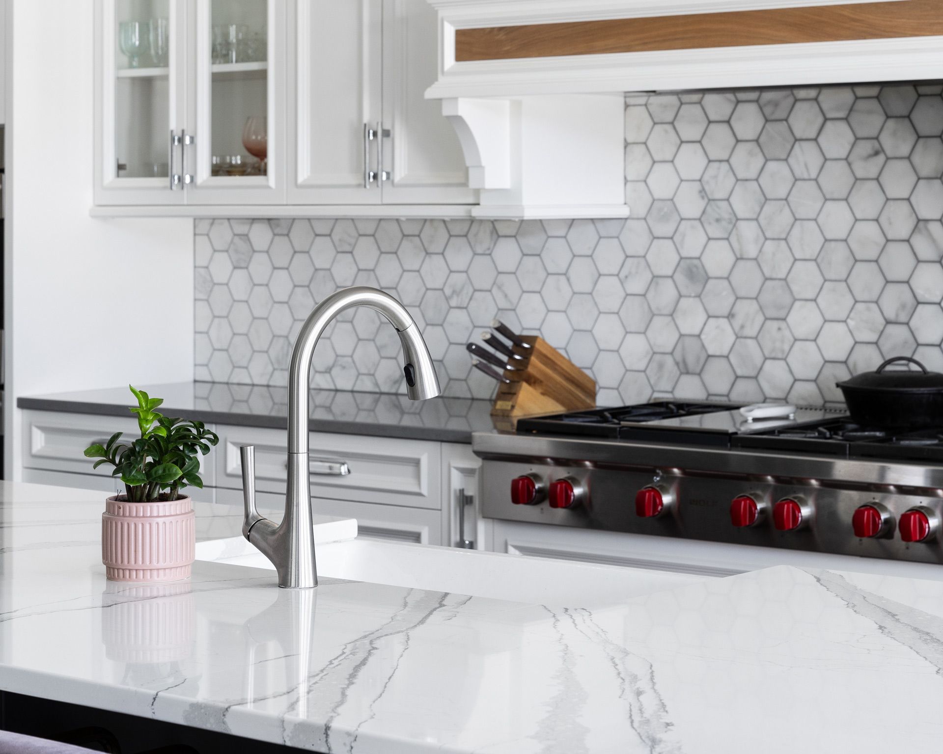 Modern white kitchen with marble island, chrome faucet, gray hex tile backsplash, and stainless steel stove