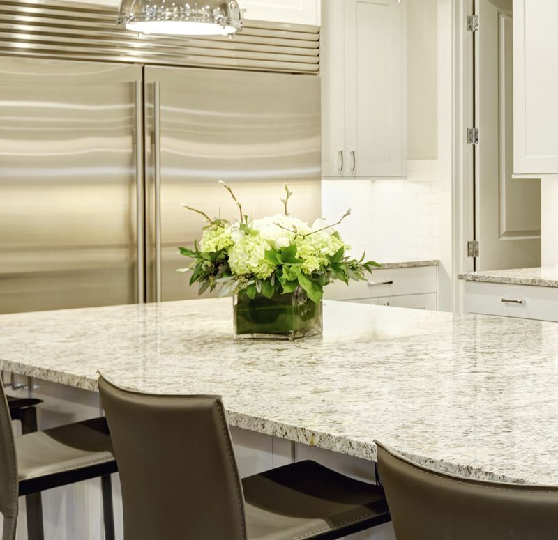 Modern kitchen with stainless steel fridge, white cabinets, marble island, and flower centerpiece