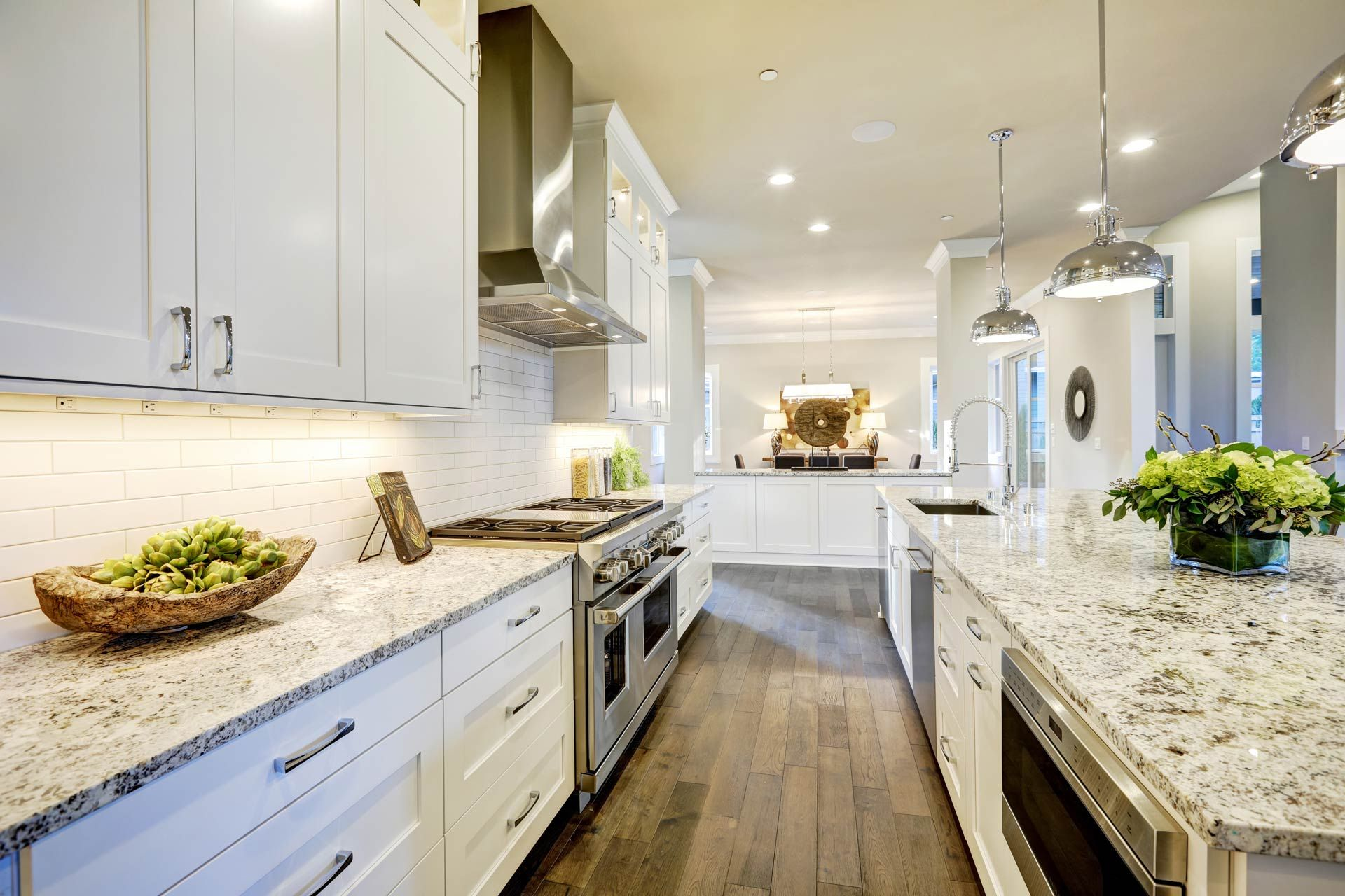 Bright modern kitchen with white cabinets, granite counters, and a large island with flowers.