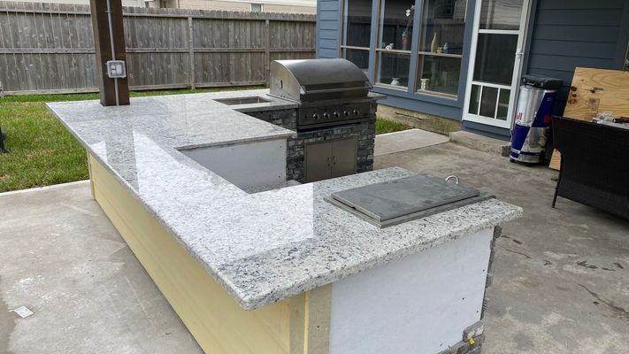 Outdoor backyard kitchen island with granite countertop and built-in grill on a concrete patio
