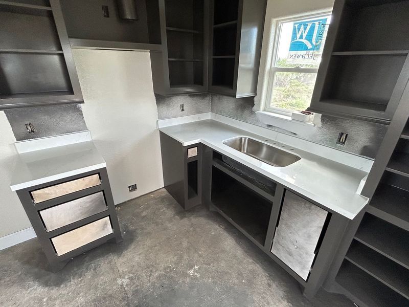 Empty kitchen with dark cabinets, white countertops, sink, and a window over the counter.