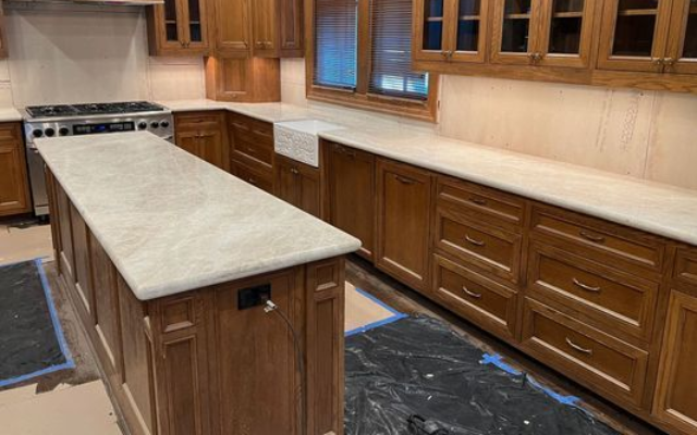 Wooden kitchen with long marble island, cabinets, and stove in the background