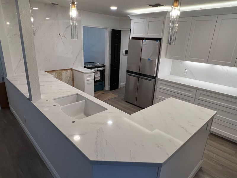 Modern white kitchen with marble-look island, stainless steel fridge, gray cabinets, and pendant lights