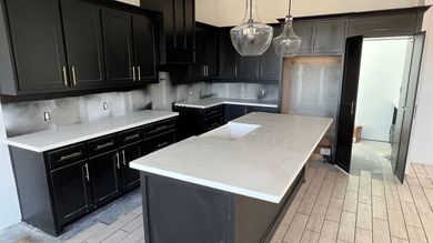 Modern kitchen with black cabinets, white countertops, stainless appliances, and a central island