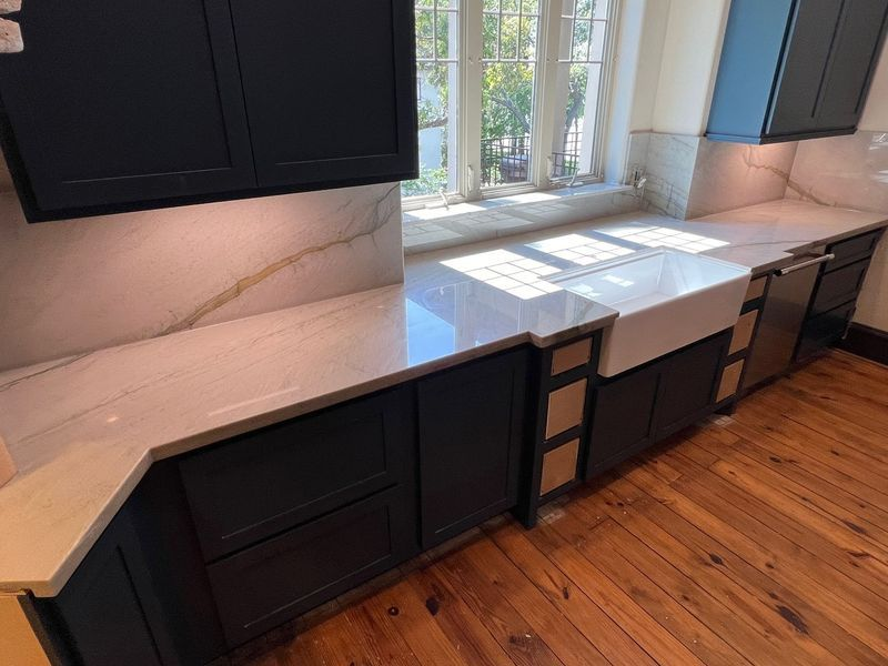 A kitchen featuring dark blue cabinets, white marble-patterned countertops, a farmhouse sink, and hardwood floors.