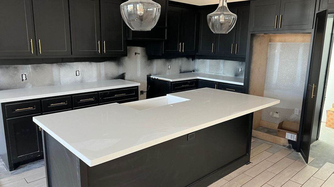 Modern kitchen with dark cabinets, white countertops, a center island with a sink, and two pendant lights.
